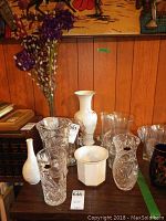 Front view of multiple vases arranged on a table against wooden panel wall with books and artwork in background.