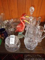 Overview photo showing two large crystal jugs with cut designs, crystal decanter with stopper, small crystal jug, hand-blown glass birds, and various bowls on a wooden surface.