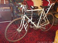 Full view of the white Raleigh men's road bike with drop handlebars and flat tires, placed indoors on a red patterned carpet.
