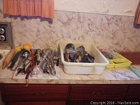 Countertop with a large collection of assorted kitchen utensils including spoons, forks, ladles, graters, spatulas, and a wooden rolling pin organized in trays and loose on counter.