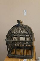 Front view of the wooden bird cage showing metal bars, dome top, and metal hanger.