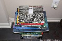 Stack of hardcover books with various titles visible including Houston, The Ultimate Gardening Book, Essential Monet, and Claude Monet