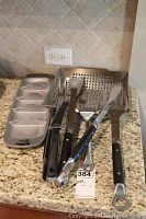 Grilling utensils and accessories displayed on granite countertop including trays and utensils.