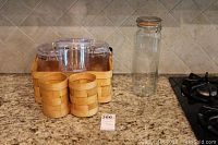 Woven bamboo picnic basket with three glass canisters inside and two bamboo utensil holders on the side, all placed on kitchen countertop.