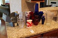 Overview of all vases and candy dishes on a kitchen countertop, includes multiple colored glass vases and two clear tall vases, one in original Waterford box.