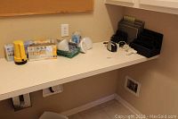 Room corner with three desktop organizers, various light bulbs, flashlight, small electronics on a white countertop.