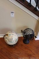 Photo showing both globes side by side on wooden floor against wall under staircase.