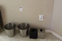 Four bathroom items placed on floor: two silver metal trash bins, one black ceramic tissue box, one silver metal tissue box.