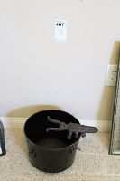 Black iron kettle with decorative ladle holder visible on the rim, shown upright on carpet in front of wall.