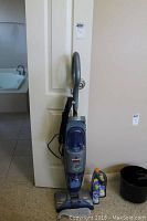 Full view of Bissell Flip It hard floor cleaner vacuum standing upright against a door with cord wrapped and mop pad attached at bottom.