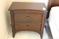Front view of a dark wooden night stand with two drawers closed, showing curved drawer fronts and small round knobs.