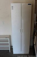 Closed view of the white utility cabinet showing the double doors with simple handles, standing against a plain wall.
