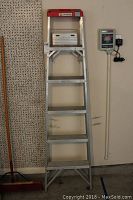 Full view of the aluminum Cuprum step ladder standing upright against a wall with six steps and red top caps.