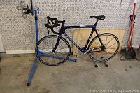 Entire bicycle mounted on blue Park Tool repair stand and silver floor stand in garage