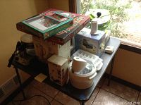 Overview of a table with several small kitchen appliances and accessories, including boxes and tools.