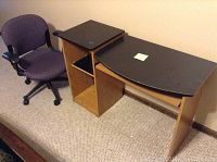 Photo showing computer desk with black top and wooden shelves next to purple swivel office chair on carpet