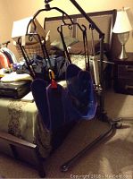 Full body sling in blue fabric attached to black metal frame with wheels and vertical support bars, shown in bedroom setting.