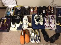 Wide view of multiple pairs of men’s shoes arranged on carpet, including dress shoes, casuals, and athletic styles in various colors and sizes.