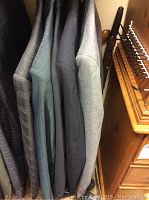 Five men's suit jackets hanging, visible in various shades of grey and blue tones, showing the fabrics and colors.