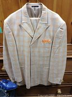 Beige and orange plaid suit jacket with notch lapel and orange pocket square hanging against wooden background.