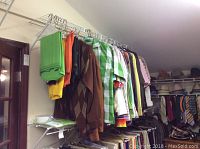 Full rack of assorted men's shirts and sweaters hanging on a white metal clothing rack showing a variety of colors including green, brown, plaid and solid tones.