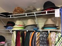 Shelf with multiple men's summer and winter hats including fabric fedoras with patterned bands in various colors. Below hats, assorted men's ties with various patterns and colors hanging on rack.