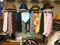 Photo showing multiple men's neckties hanging on a rack in various colors and patterns along with a few hats on top shelf.