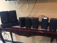 Photo showing six black speakers of various sizes arranged on a wooden piece of furniture, all with fabric covers, some with visible Infinity logos.