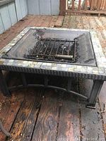 View of square fire pit with metal grate and tiled edge, showing condition and construction.