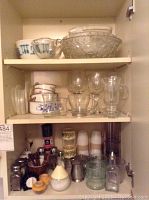 Wide view of cupboard shelf with ceramic cups and textured glass serving bowls