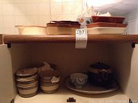 Kitchen pottery items arranged on a shelf showing covered bean pot, dishes, and stacked bowls.