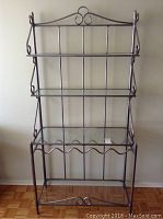 Front view of the metal framed baker's rack with glass shelves and wine bottle holder.