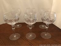 Six large red wine glasses arranged on a dark wooden surface, clear crystal with pinwheel cut pattern on the bowl and long stems.