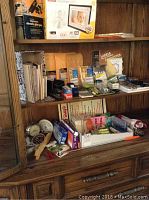 Wide shot of the wooden shelf with assorted office items including digital photo frame box, glue gun box, envelopes, labels, and office stationery items.