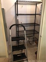 Photo showing black metal wire shelving unit and black three-step stool with curved handle