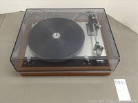 Full top-front view of turntable with closed acrylic dust cover over walnut plinth and aluminum deck