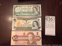Top view of the 1967 Centennial One Dollar note, 1969 One Dollar, and 1975 Two Dollar Canadian banknotes arranged vertically on a table.