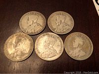 Top view of five Canadian quarters from 1920, 1928, 1930, 1931, and 1934 laid out on a wooden surface.