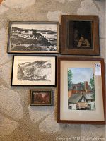 Five framed artworks arranged on carpet, showing variety of sizes and styles including a black and white photo print, sketch, and paintings.