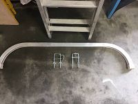 Curved stabilizer bar and two U-shaped bumpers for ladder attachment shown on a concrete floor.