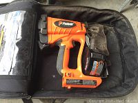 Photo of orange and black Paslode cordless roofing coil nailer inside soft carry bag, showing nail gun with coil magazine and ergonomic handle.