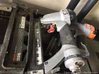 Photo showing a metal air nailer with red trigger and pneumatic fittings