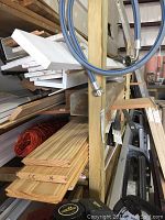 Shelves showing assorted wood planks, white foam panels, plastic strips, and metal pieces organized in a workshop.