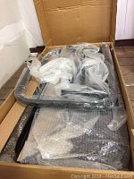 Box containing multiple metal components wrapped in plastic and bubble wrap, parts of rear flip seat frame for golf cart.