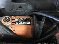Orange electric saw model R300 inside black carrying case with power cord wrapped around it.