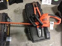 Full view of the Black & Decker hedge trimmer laid on a black tool case showing orange body with blade and handle grips.