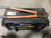 Bolt cutters with orange handles placed on top of a black Bostitch toolbox.
