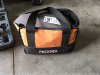 Soft-sided Ridgid carrying case in gray and orange with black straps and Ridgid logo on side.