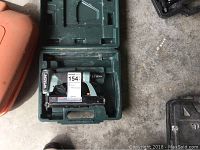 Green Hitachi pneumatic nailer inside green molded carrying case, showing the full tool in the case.