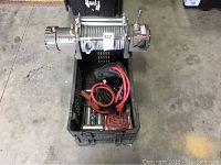 Electric winch in a plastic crate showing steel cable spool and battery clamp cables